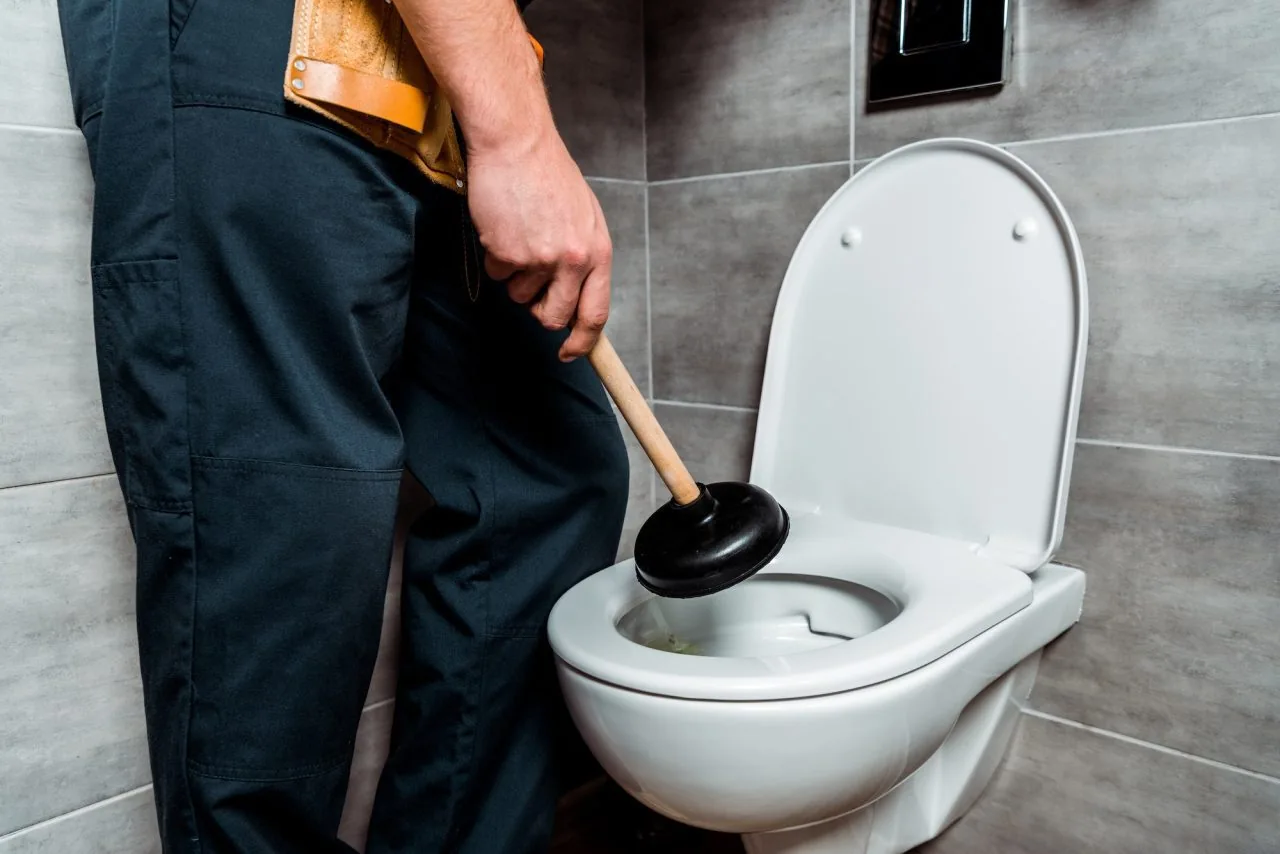 Plumber holding a plunger beside a toilet